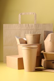 Photo of Eco friendly food packaging. Paper containers, tableware and bag on pale yellow background