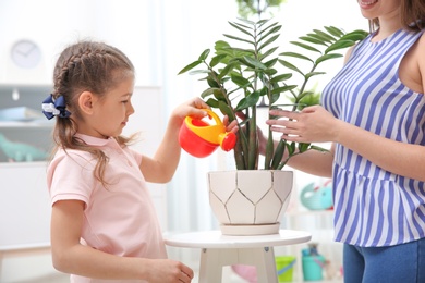 Child with toy watering can helping mother to take care of houseplant at home. Playing indoors