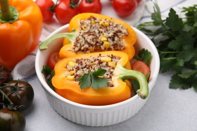 Photo of Quinoa stuffed bell pepper, tomatoes and parsley in bowl on light table, closeup