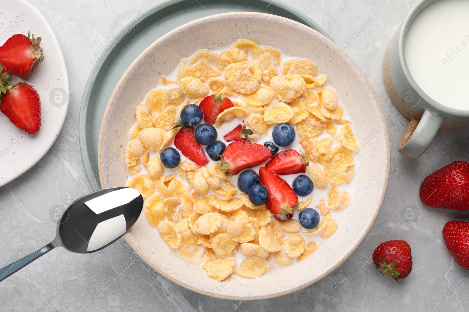 Photo of Bowl of tasty crispy corn flakes with milk and berries on light grey table, flat lay