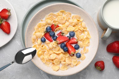 Bowl of tasty crispy corn flakes with milk and berries on light grey table, flat lay