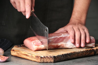 Photo of Man cutting fresh raw meat on grey table, closeup