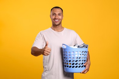 Photo of Happy man with basket full of laundry showing thumb up on orange background