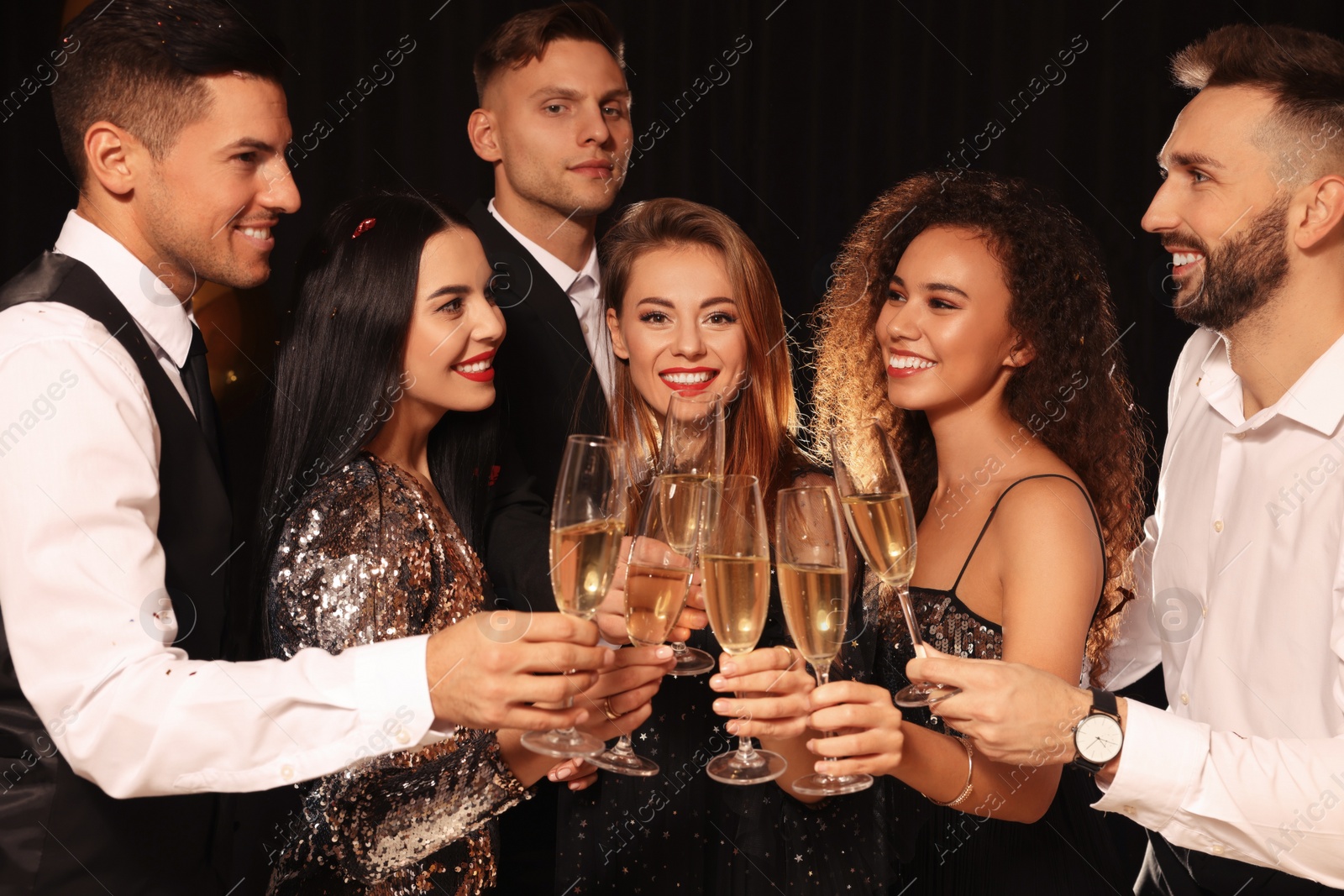 Photo of Happy friends with glasses of sparkling wine celebrating New Year on black background