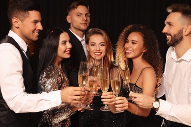 Happy friends with glasses of sparkling wine celebrating New Year on black background