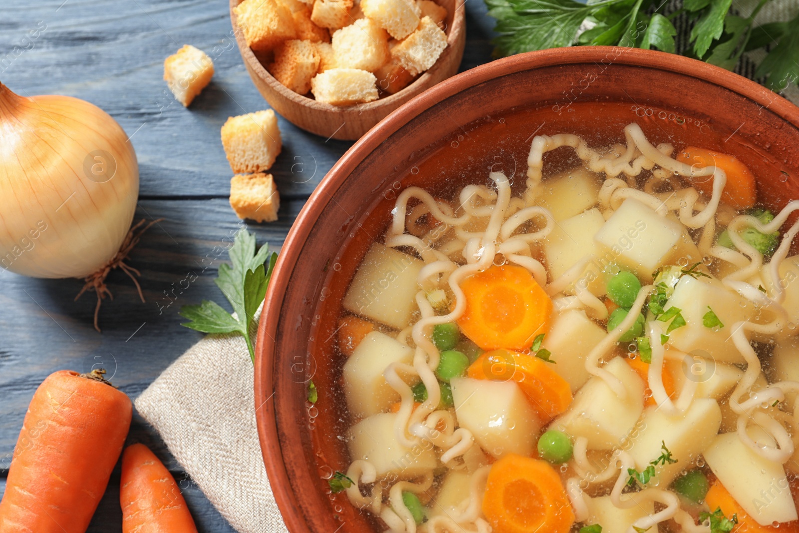 Photo of Bowl of fresh homemade vegetable soup with ingredients on blue wooden table, flat lay