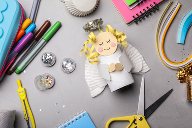 Toy angel made of toilet paper hub among stationery on grey table, flat lay