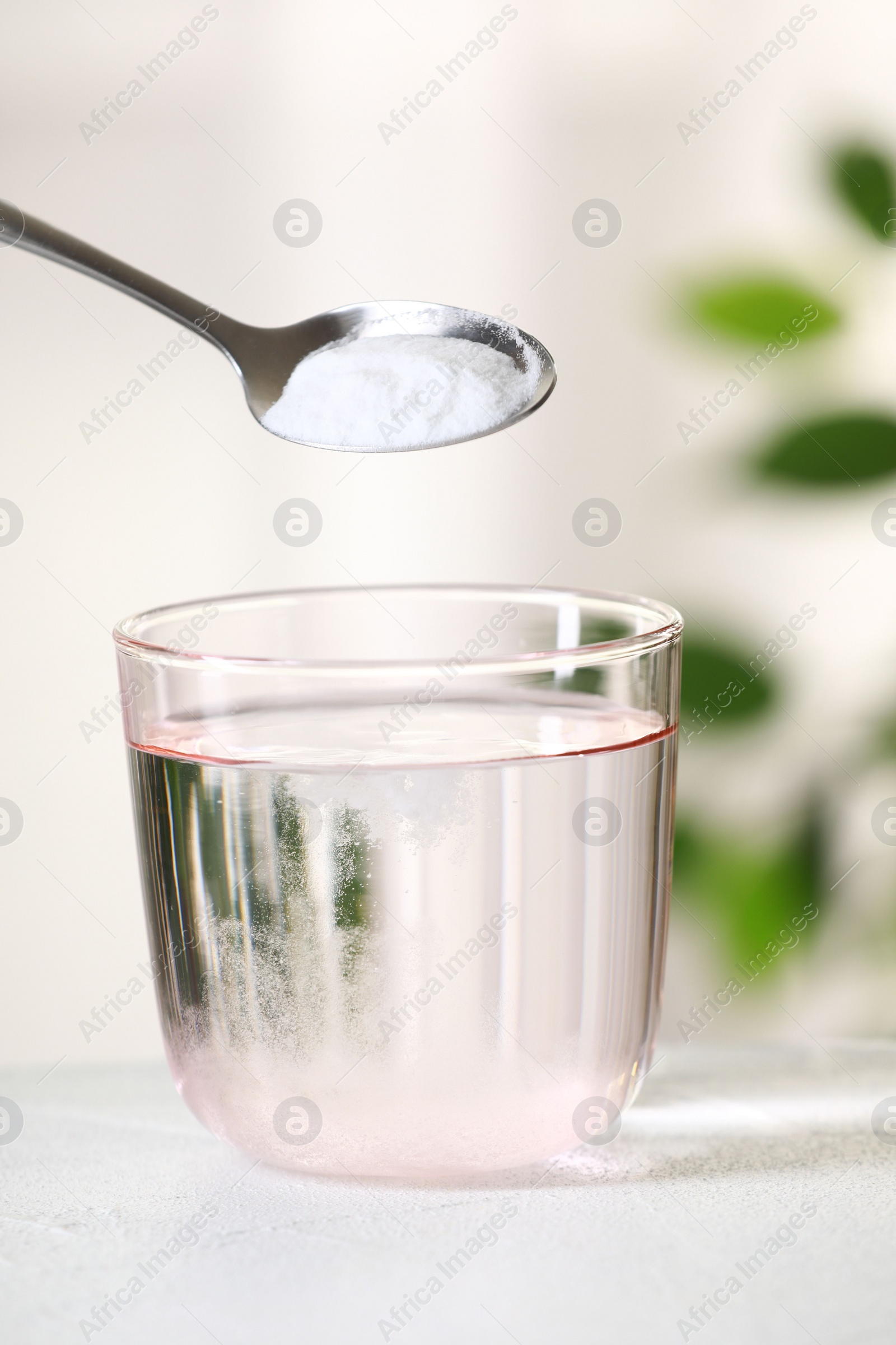 Photo of Adding baking soda into glass of water at white table against blurred background