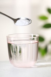 Adding baking soda into glass of water at white table against blurred background