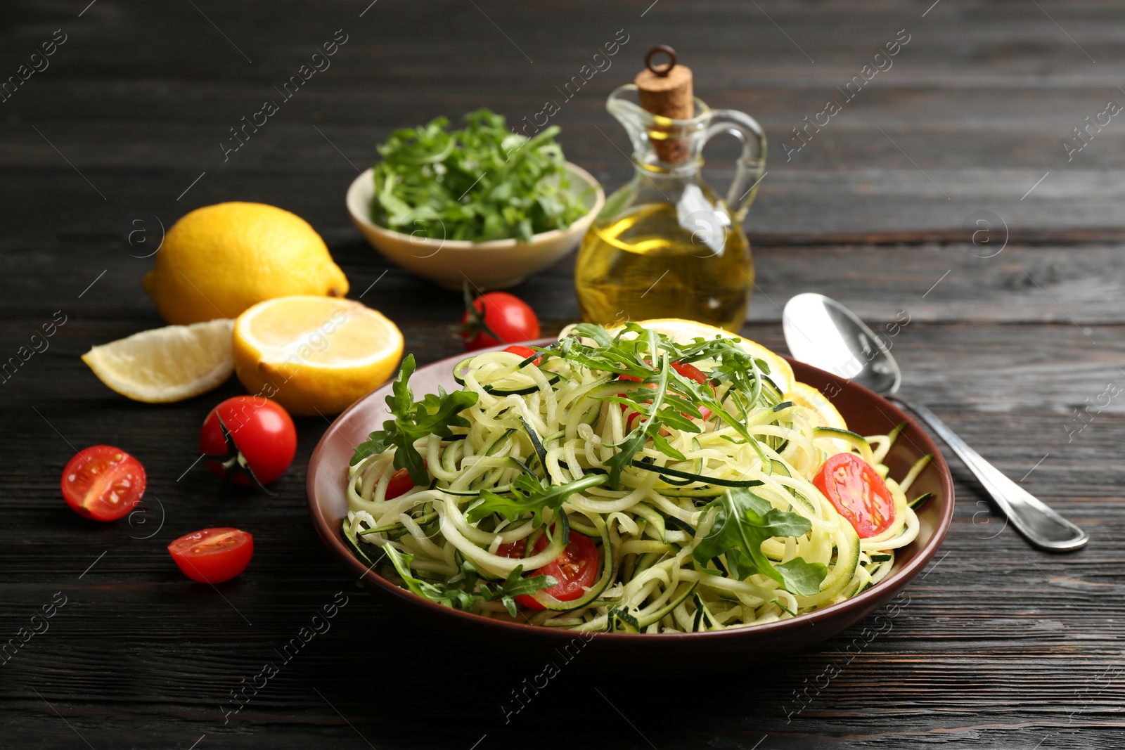 Photo of Delicious zucchini pasta with cherry tomatoes and arugula served on black wooden table