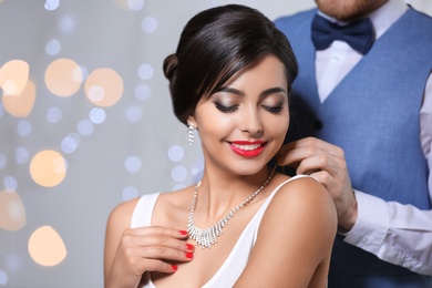 Man putting elegant jewelry on beautiful woman against blurred background. Space for text