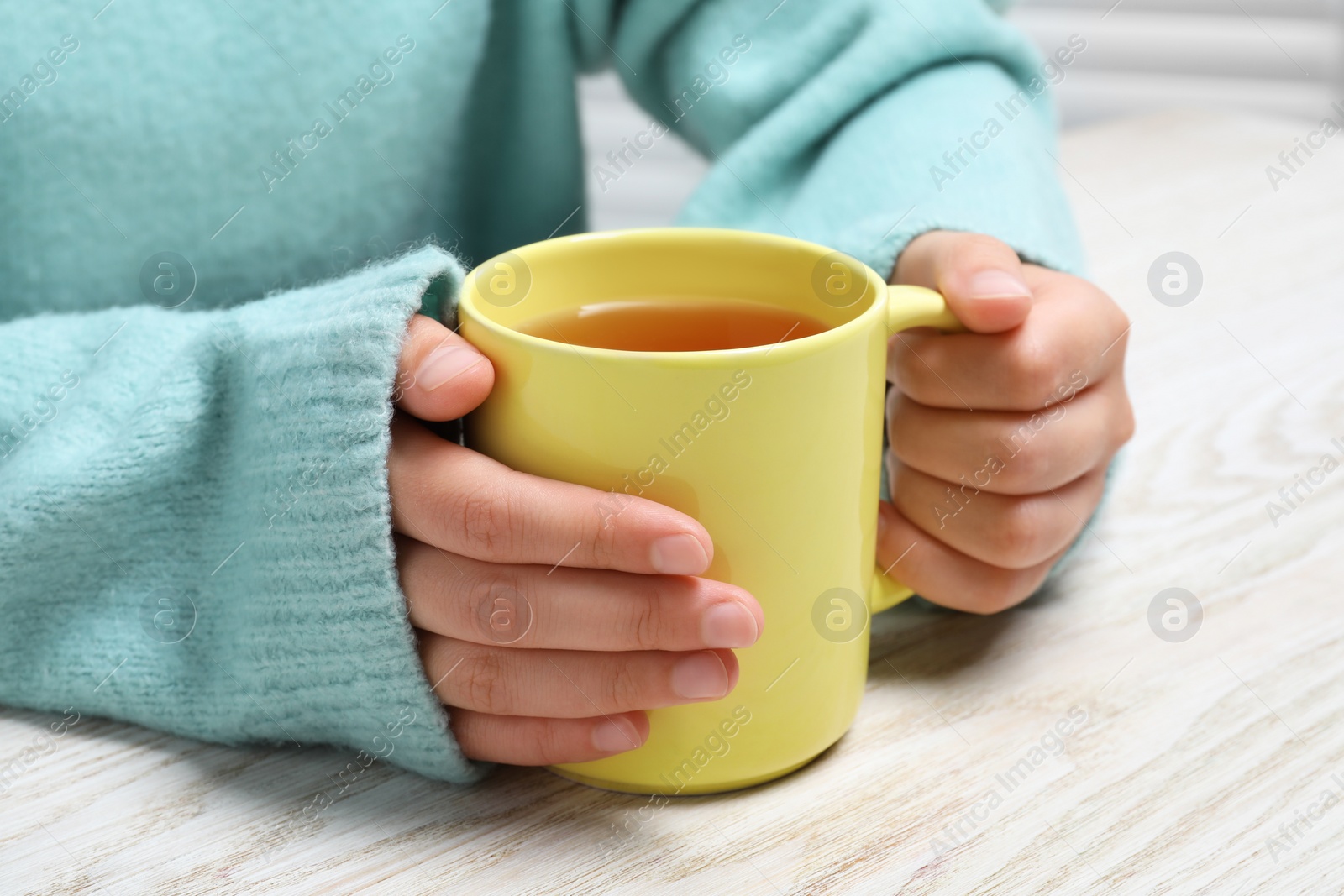 Photo of Woman holding mug of tea at wooden table, closeup