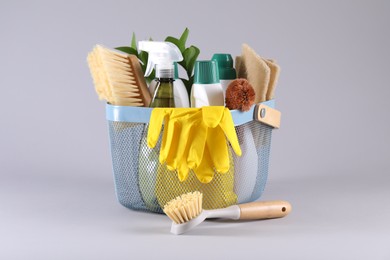 Set of different cleaning supplies in basket on light grey background