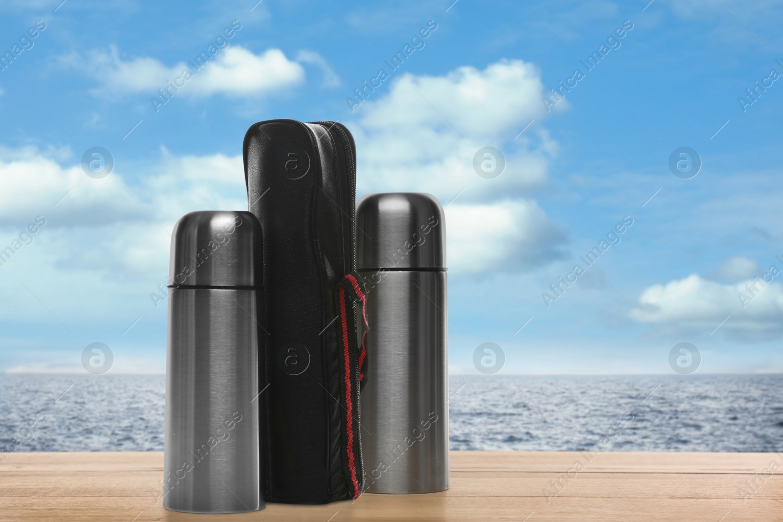 Image of Thermoses on wooden table near sea under blue sky