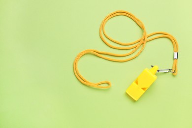 Photo of One yellow whistle with cord on light green background, top view. Space for text
