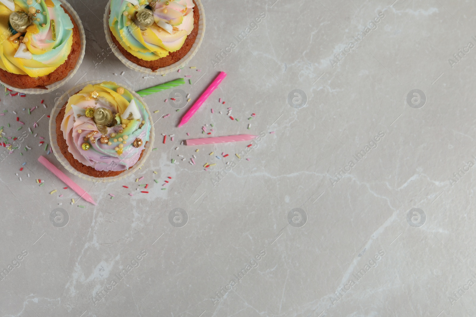 Photo of Cute sweet unicorn cupcakes on beige marble table, flat lay. Space for text