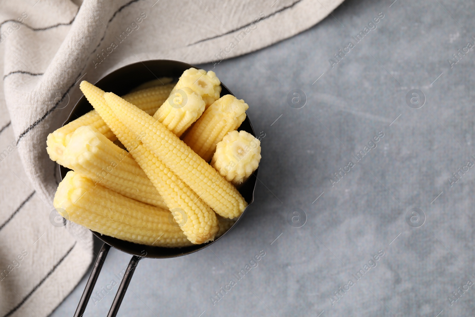 Photo of Tasty fresh yellow baby corns in dish on grey table, top view. Space for text