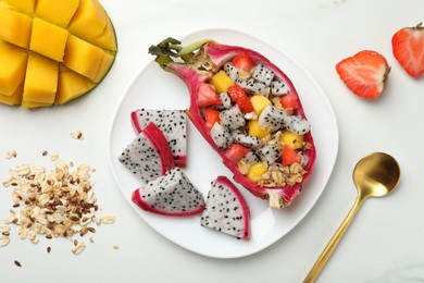 Yummy pitahaya boat with mango, granola and strawberry on white table, flat lay