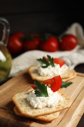 Photo of Delicious crackers with cream cheese, tomato and parsley on wooden board, closeup