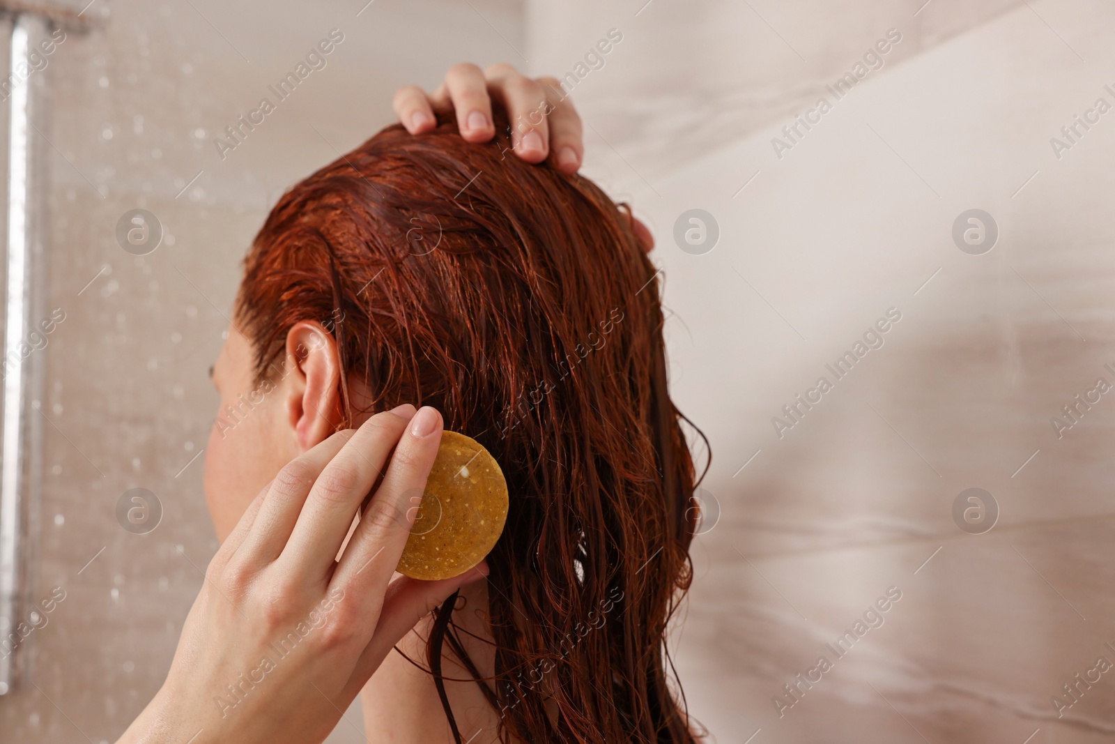 Photo of Young woman washing her hair with solid shampoo bar in shower, back view