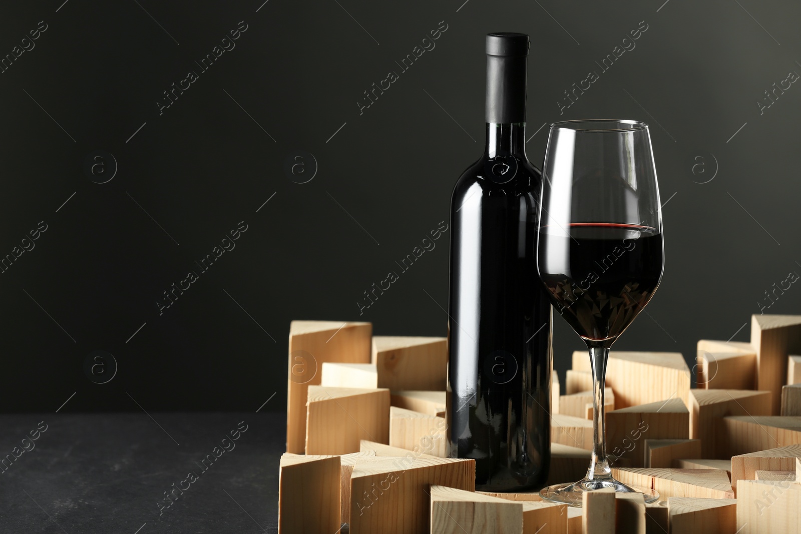 Photo of Stylish presentation of red wine in bottle and wineglass on black background, space for text