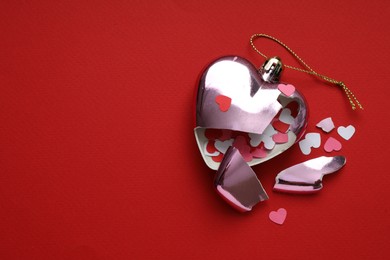 Broken heart. Crashed bauble in shape of heart with confetti on red background, top view. Space for text