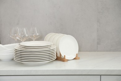 Photo of Clean plates, bowls and glasses on white marble table, space for text