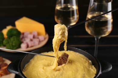 Photo of Dipping pieces of ham and bread into fondue pot with melted cheese on table, closeup