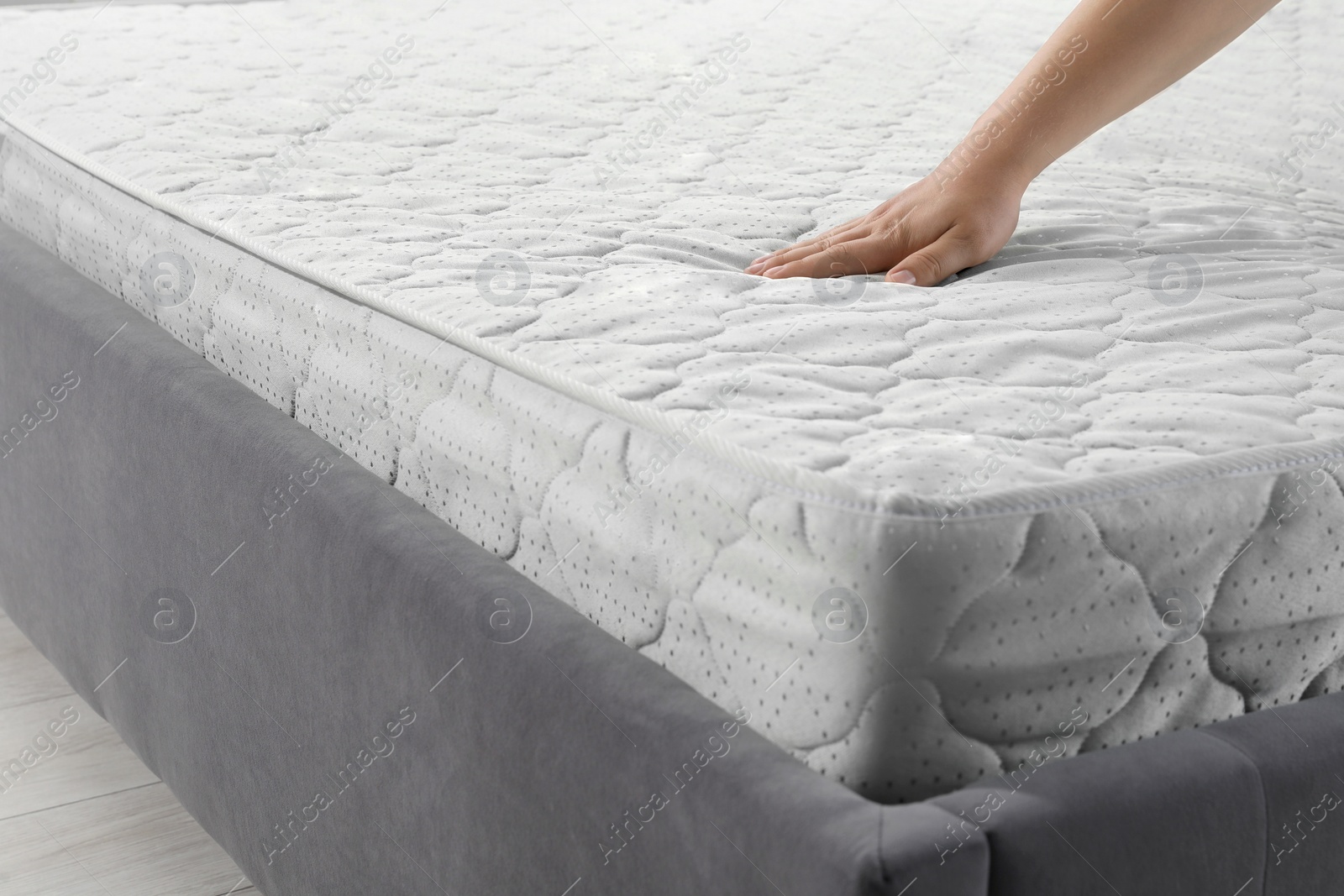 Photo of Woman touching soft light green mattress on gray bed, closeup