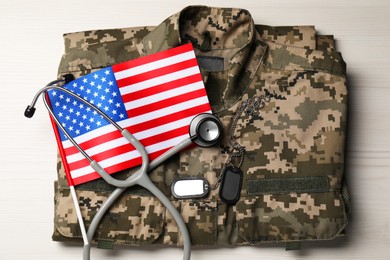 Photo of Stethoscope, USA flag, tags and military uniform on white wooden table, top view