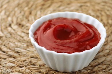 Photo of Bowl of tasty ketchup on wicker mat, closeup