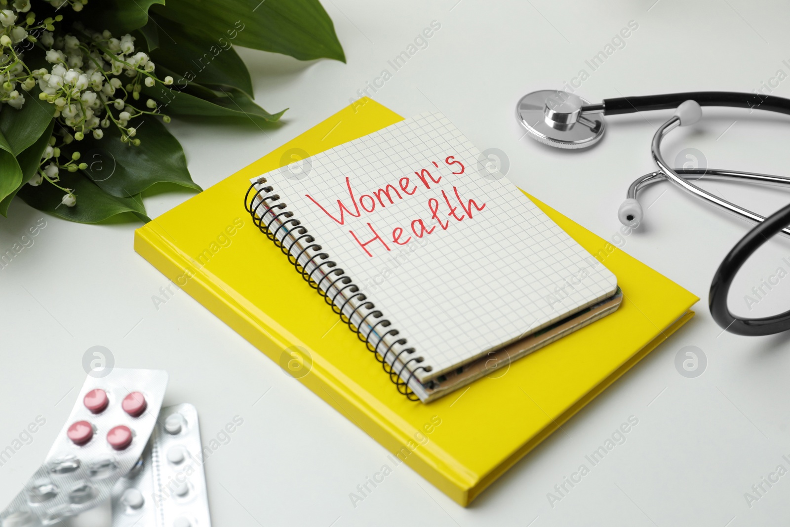 Photo of Notebook with text Women's Health, pills and stethoscope on white table