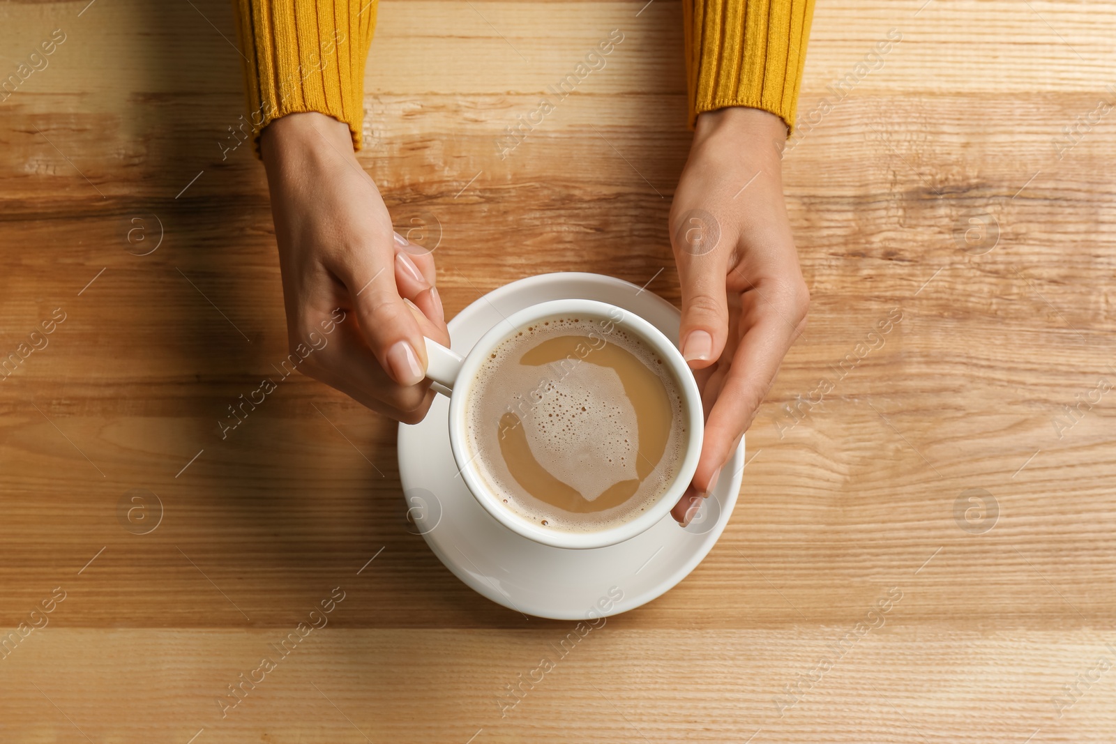 Photo of Woman holding cup of coffee at wooden table, top view