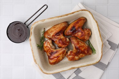 Photo of Fresh marinade, chicken wings and rosemary on white tiled table, top view