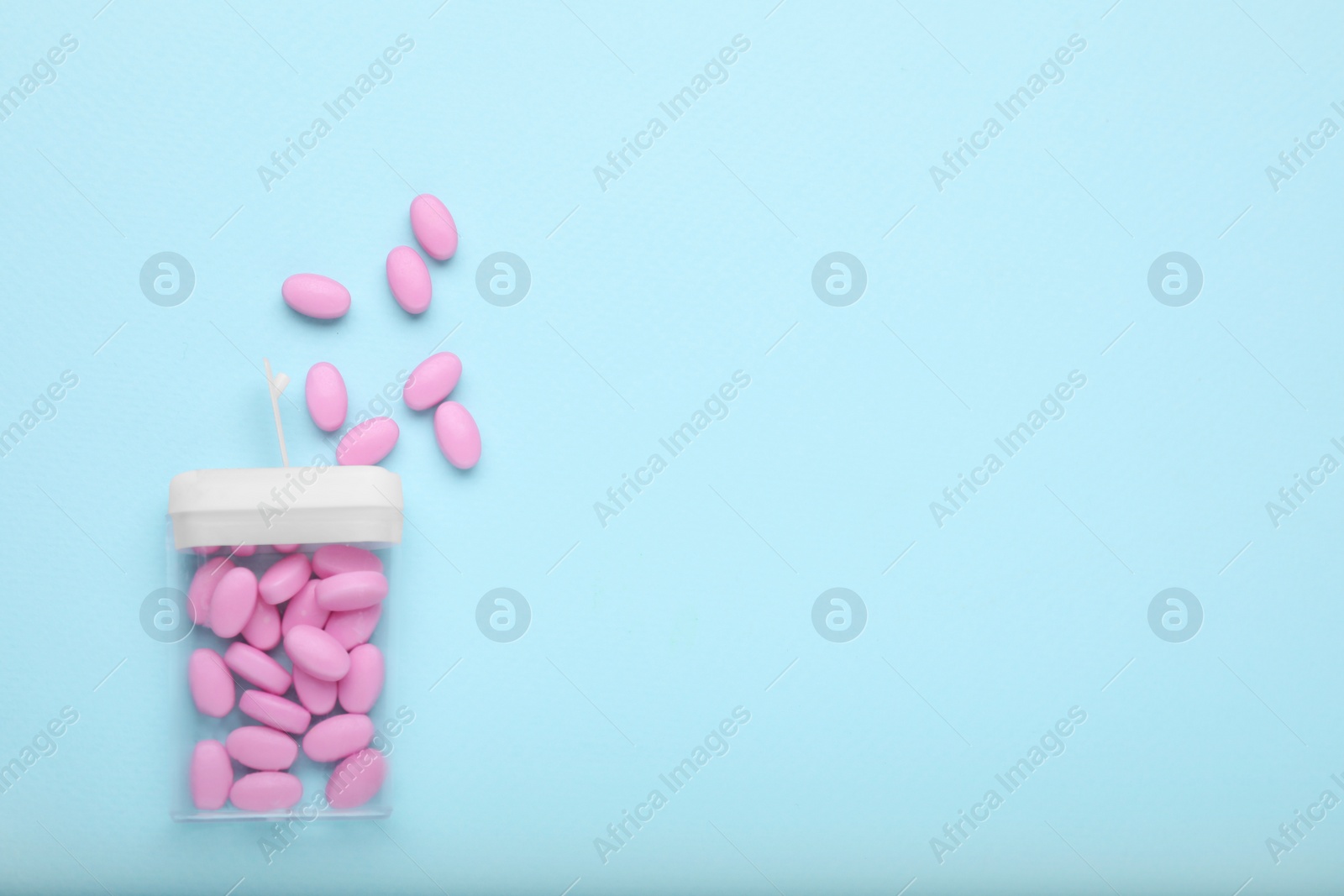 Photo of Tasty pink dragee candies and container on light blue background, flat lay. Space for text