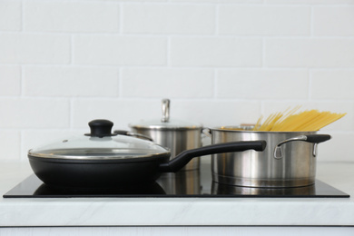 Photo of Pot with uncooked pasta and frying pan on stove in kitchen