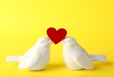 Photo of Ceramic birds holding little heart on color background