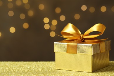 Photo of Beautiful gift box on golden table against blurred festive lights, space for text