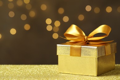 Beautiful gift box on golden table against blurred festive lights, space for text