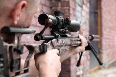 Photo of Soldier holding modern powerful sniper rifle with telescopic sight outdoors, closeup