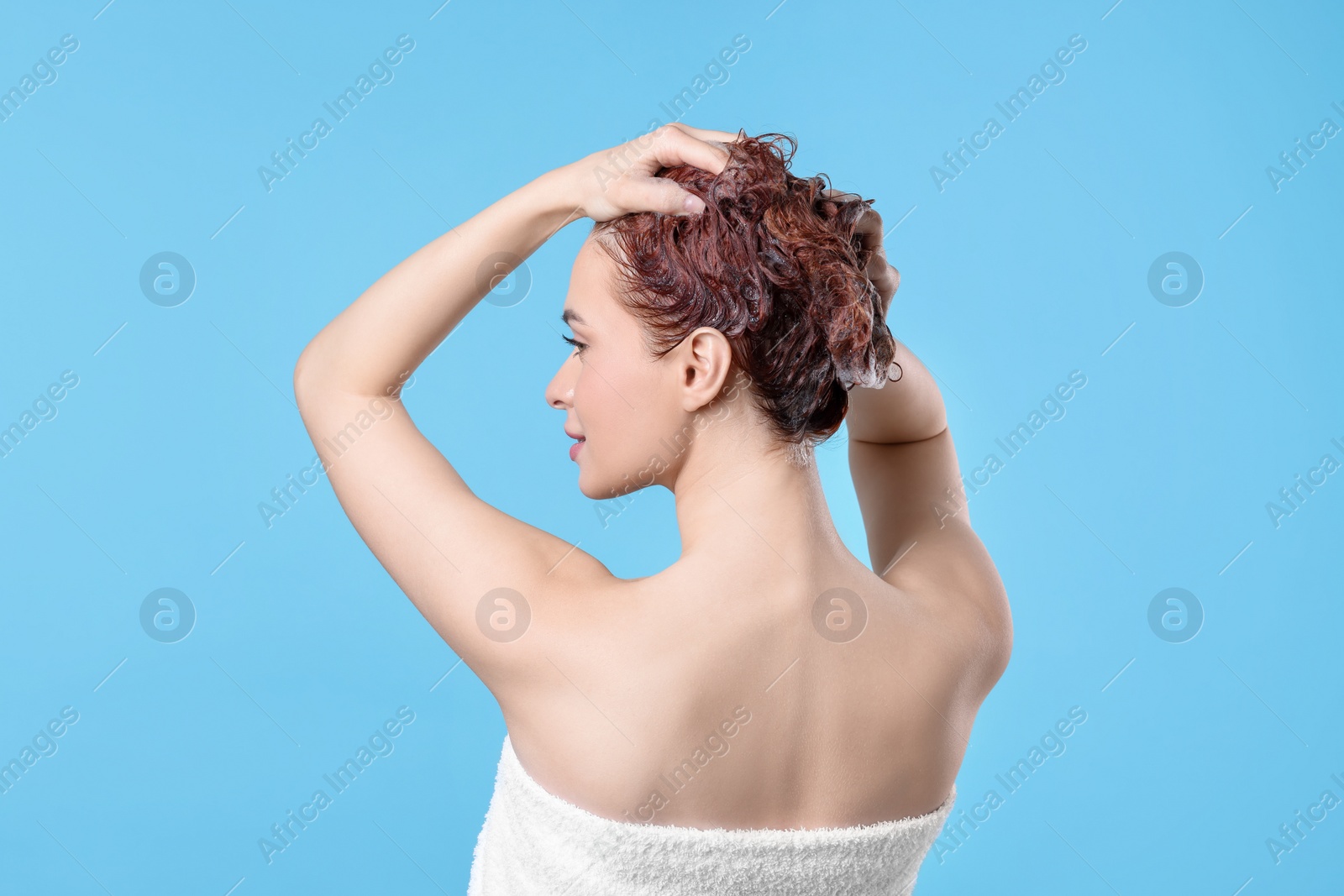 Photo of Young woman washing her hair with shampoo on light blue background, back view