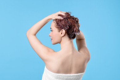 Photo of Young woman washing her hair with shampoo on light blue background, back view