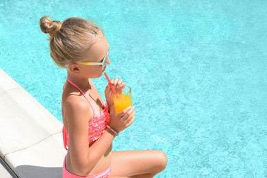 Cute little girl with glass of juice in swimming pool on sunny day. Space for text