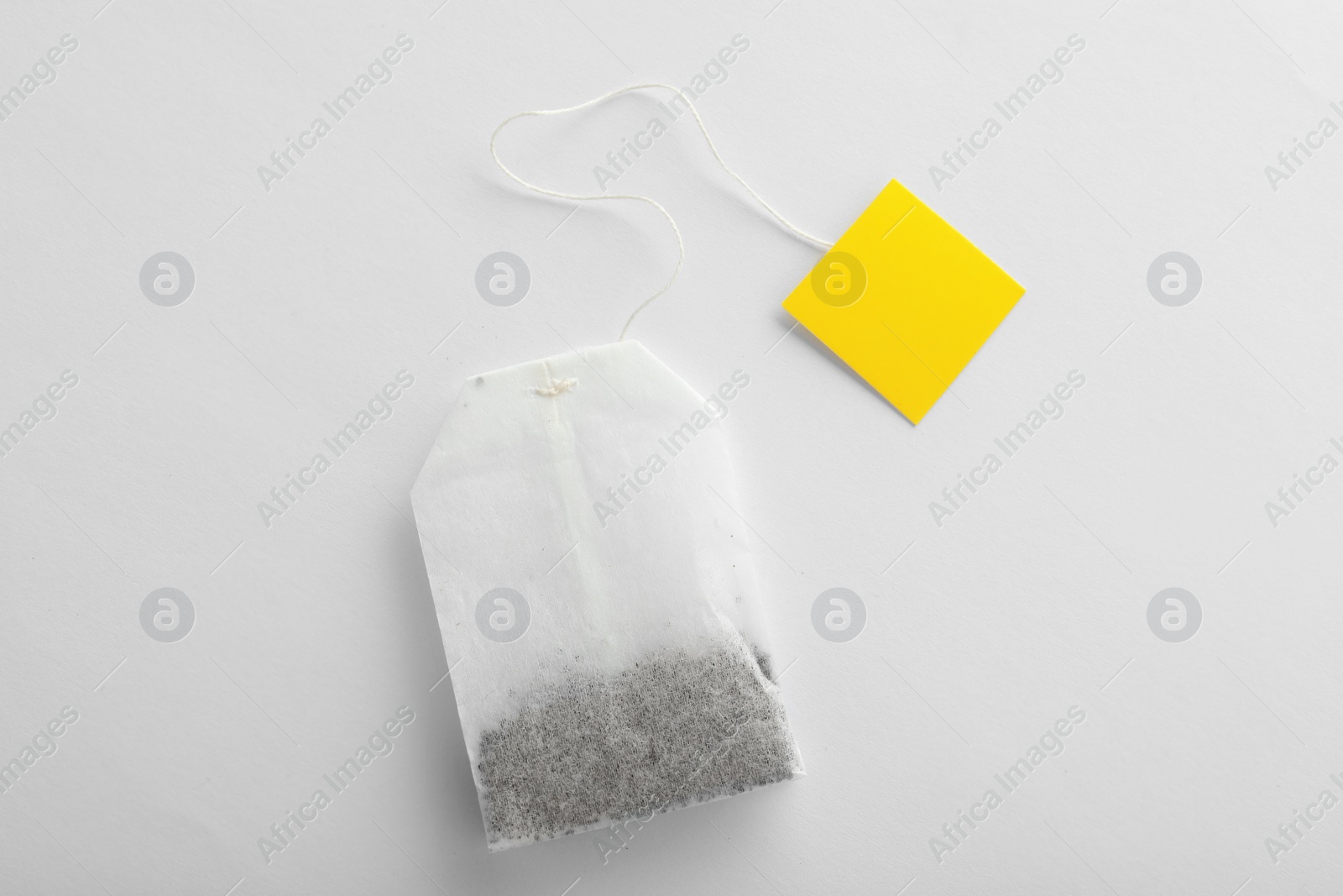 Photo of Unused tea bag with tag on white background, top view. Space for text