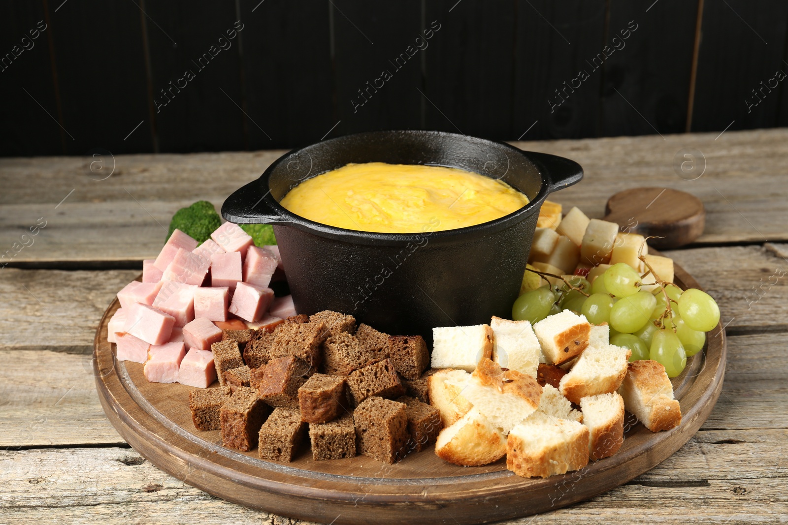 Photo of Fondue pot with melted cheese and different products on wooden table