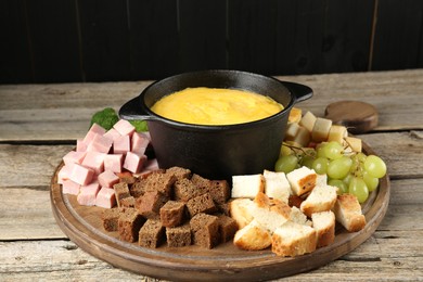 Photo of Fondue pot with melted cheese and different products on wooden table