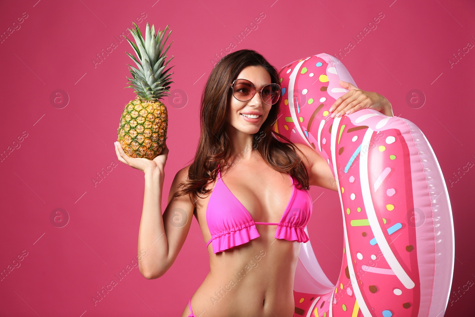 Photo of Beautiful woman in stylish bikini with inflatable ring and pineapple on crimson background