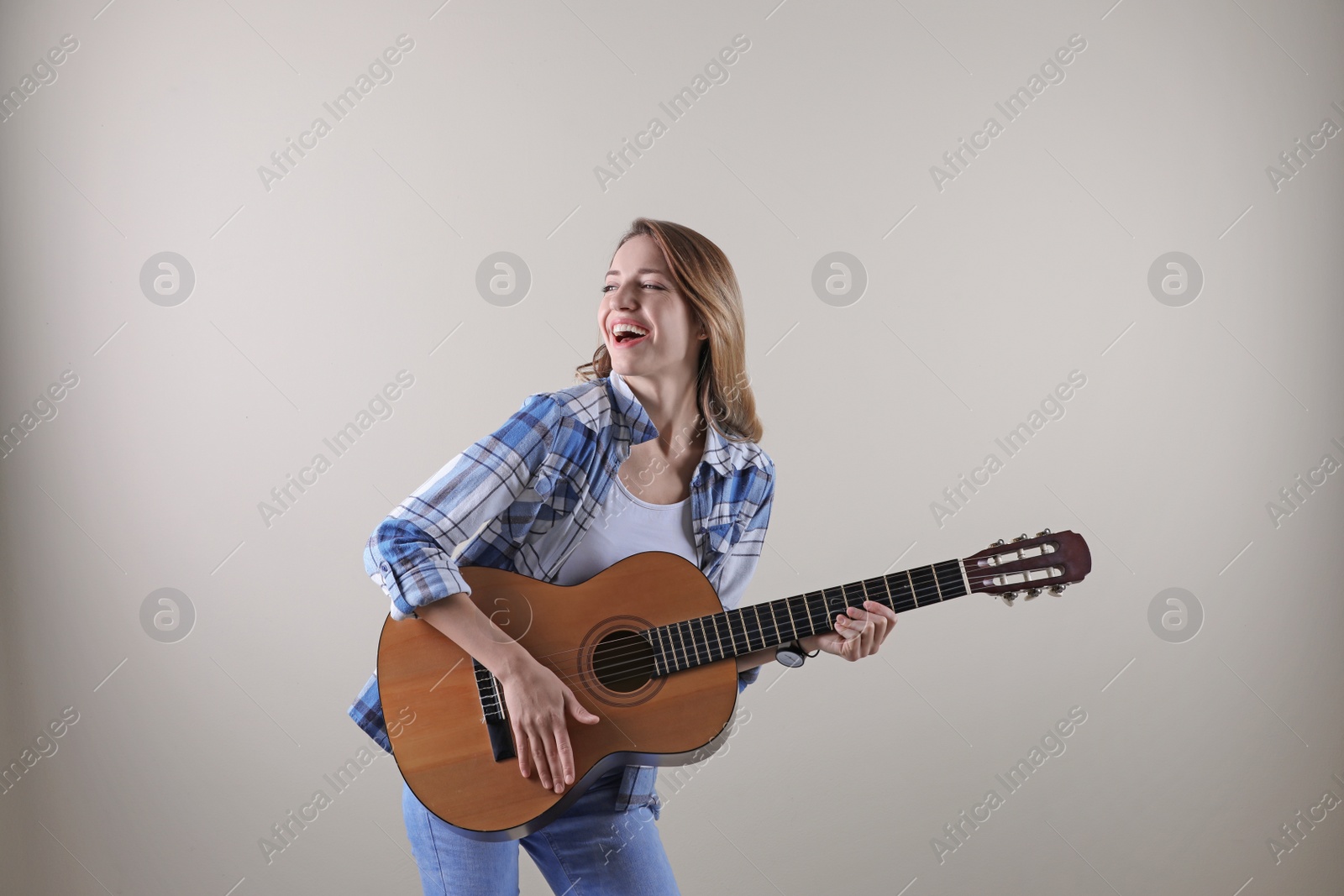 Photo of Young woman playing acoustic guitar on grey background