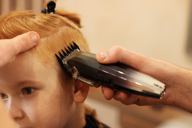 Photo of Professional hairdresser cutting boy's hair in beauty salon, closeup