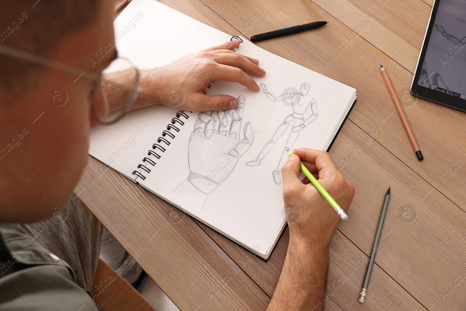 Photo of Man drawing in sketchbook with pencil at wooden table, closeup